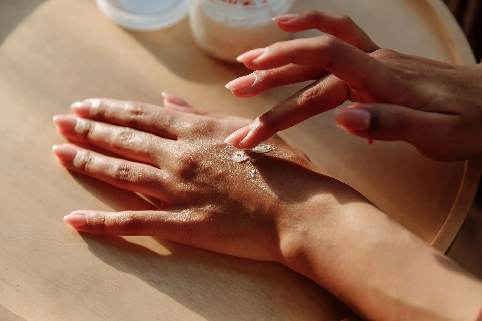 Duas mãos com tons de pele diferentes espalhando creme sobre a pele